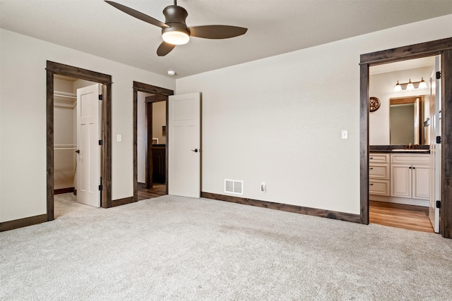 unfurnished bedroom with sink, ensuite bathroom, light colored carpet, and a walk in closet