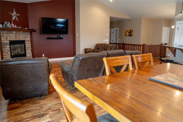 dining area with a stone fireplace, wood-type flooring, and vaulted ceiling