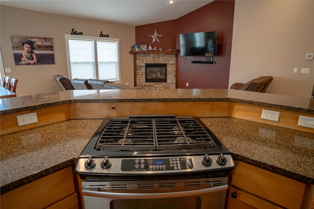 kitchen with kitchen peninsula, a fireplace, stainless steel range, and dark stone counters