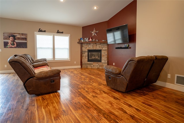 living room featuring hardwood / wood-style flooring, a stone fireplace, and lofted ceiling