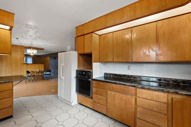 kitchen with wooden walls, black oven, an inviting chandelier, light wood-type flooring, and white fridge