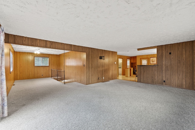 carpeted empty room with ceiling fan, a textured ceiling, and wooden walls