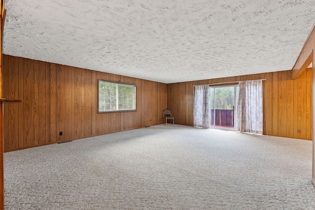 carpeted spare room featuring wood walls and a textured ceiling