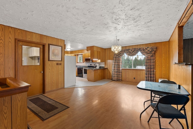 dining room featuring a textured ceiling, wood walls, an inviting chandelier, and light hardwood / wood-style flooring