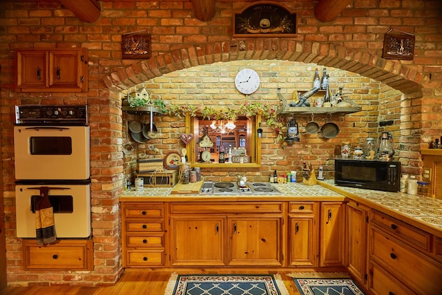 kitchen featuring brick wall, light hardwood / wood-style flooring, tile countertops, and white appliances