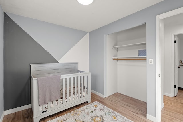 bedroom with a crib, light wood-type flooring, and a closet