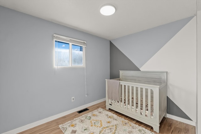 bedroom featuring lofted ceiling, a nursery area, and hardwood / wood-style flooring