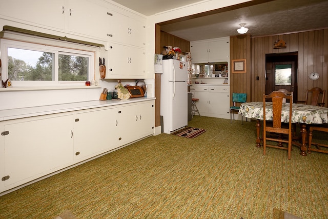 kitchen with white fridge, wood walls, white cabinetry, and dark colored carpet