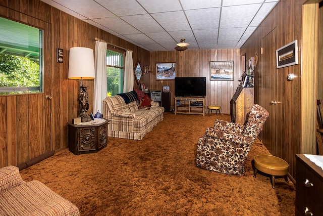 living room featuring a drop ceiling, wood walls, and carpet flooring