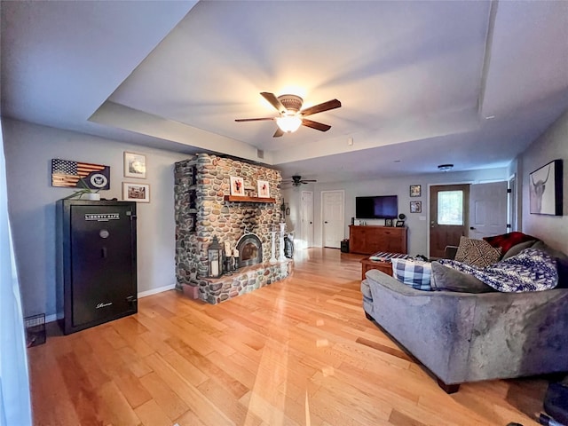 living room featuring a stone fireplace, a raised ceiling, and light hardwood / wood-style floors