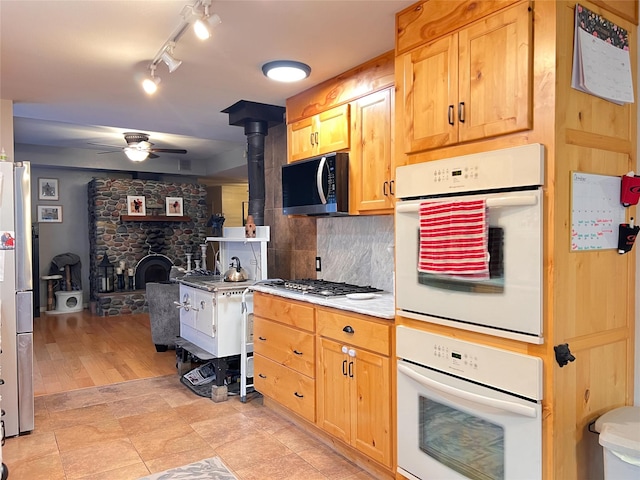 kitchen with light brown cabinets, a wood stove, appliances with stainless steel finishes, ceiling fan, and backsplash