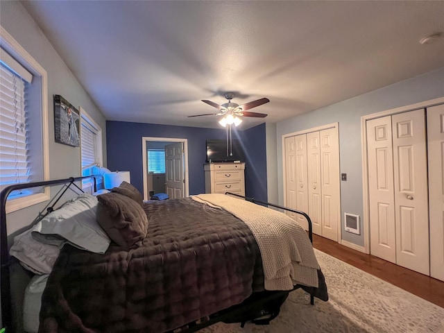 bedroom with ceiling fan, hardwood / wood-style floors, and multiple closets