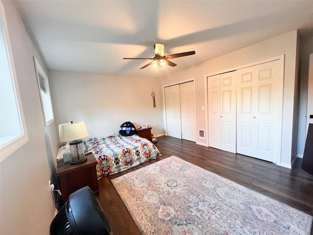 bedroom with multiple closets, dark wood-type flooring, and ceiling fan