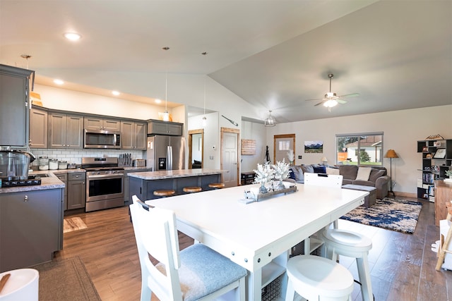 kitchen featuring a kitchen island, stainless steel appliances, gray cabinetry, hanging light fixtures, and vaulted ceiling