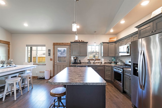 kitchen with appliances with stainless steel finishes, hanging light fixtures, a healthy amount of sunlight, and a center island