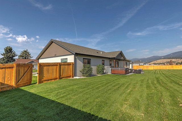 rear view of property with a mountain view, a yard, and a hot tub