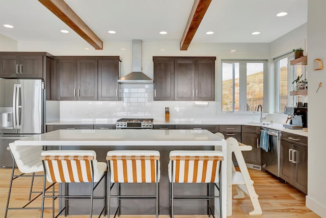 kitchen featuring beamed ceiling, a center island, stainless steel appliances, wall chimney exhaust hood, and light hardwood / wood-style floors