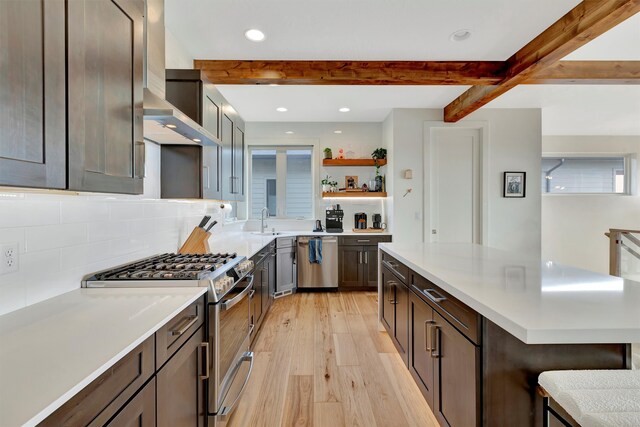 kitchen featuring beamed ceiling, wall chimney exhaust hood, backsplash, appliances with stainless steel finishes, and light hardwood / wood-style floors