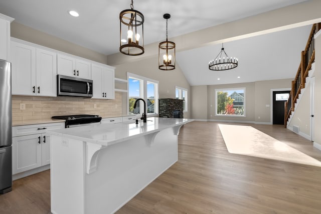 kitchen featuring light wood-type flooring, stainless steel appliances, pendant lighting, white cabinetry, and an island with sink