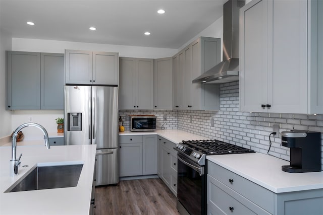 kitchen with wall chimney range hood, appliances with stainless steel finishes, sink, gray cabinets, and dark hardwood / wood-style floors