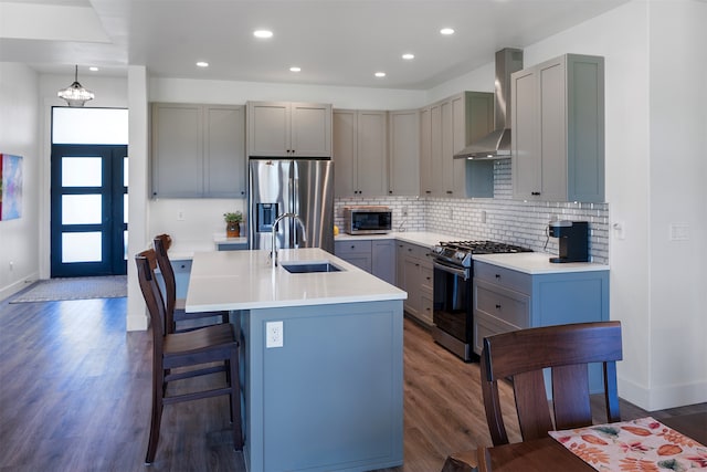 kitchen featuring a center island with sink, sink, stainless steel appliances, wall chimney exhaust hood, and dark hardwood / wood-style floors