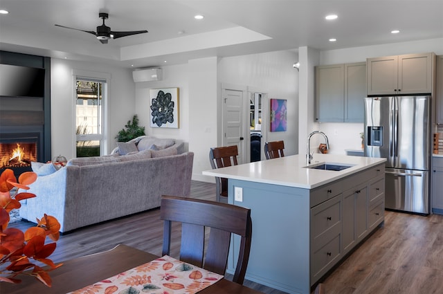 kitchen with gray cabinetry, sink, an island with sink, dark hardwood / wood-style flooring, and stainless steel fridge with ice dispenser