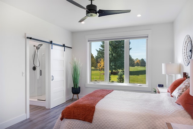 bedroom featuring ceiling fan, hardwood / wood-style flooring, ensuite bathroom, and a barn door