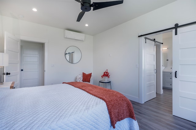 bedroom with a barn door, dark hardwood / wood-style flooring, ceiling fan, connected bathroom, and a wall mounted AC