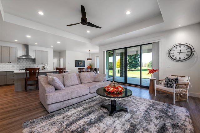 living room with ceiling fan, a tray ceiling, and dark hardwood / wood-style flooring