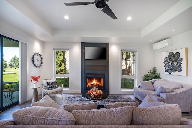 living room with an AC wall unit, a raised ceiling, hardwood / wood-style flooring, and ceiling fan