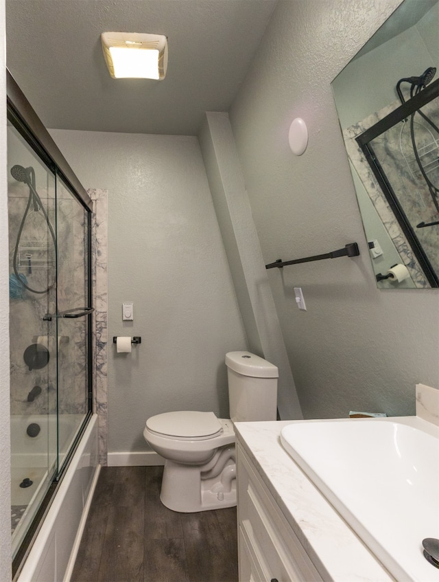 full bathroom featuring vanity, bath / shower combo with glass door, hardwood / wood-style flooring, and toilet