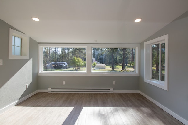 empty room featuring lofted ceiling, baseboard heating, and wood-type flooring