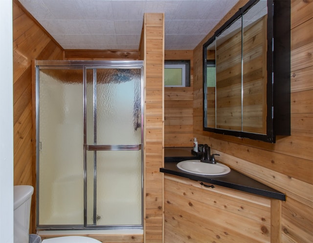 bathroom with vanity, wooden walls, a shower with shower door, and toilet