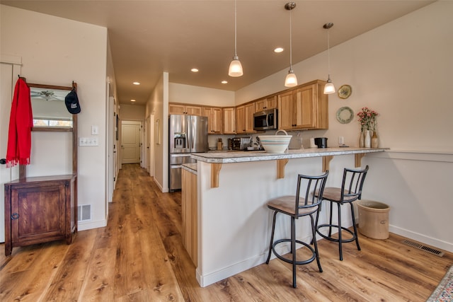 kitchen featuring kitchen peninsula, stainless steel appliances, light wood-type flooring, and a kitchen breakfast bar