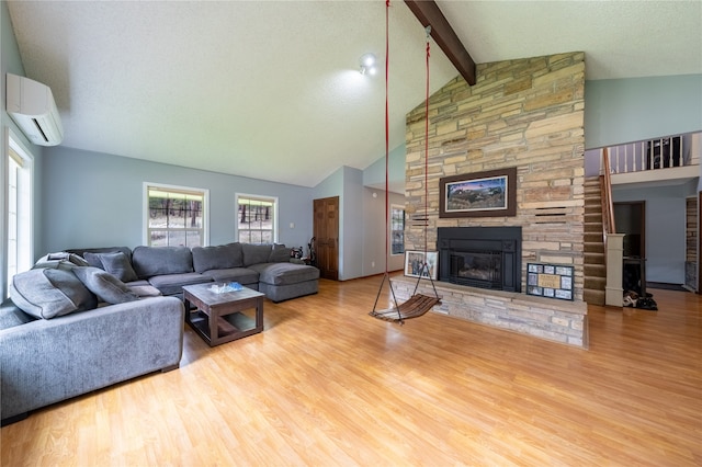 living room with a wall mounted AC, a stone fireplace, high vaulted ceiling, beamed ceiling, and light hardwood / wood-style floors