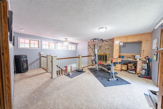 exercise area featuring a textured ceiling, a fireplace, light colored carpet, and ceiling fan