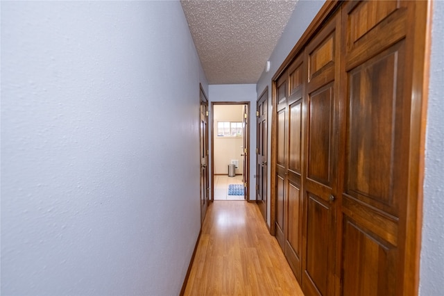 hall with a textured ceiling and light wood-type flooring