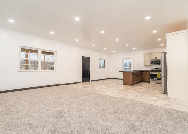 kitchen featuring cream cabinets, a center island, light colored carpet, and appliances with stainless steel finishes