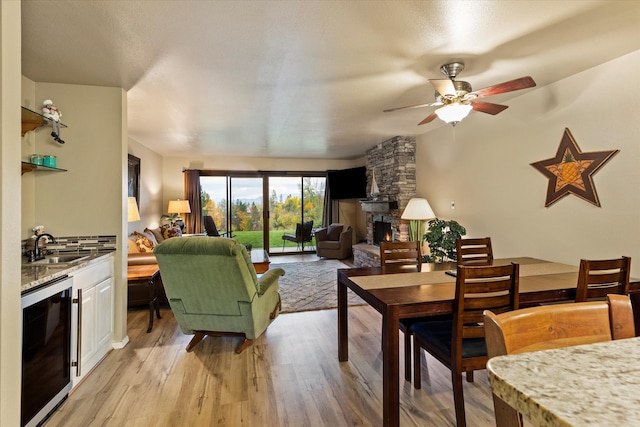 living room featuring light hardwood / wood-style floors, wine cooler, a fireplace, and ceiling fan