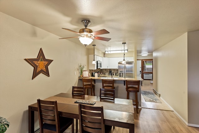 dining area featuring a wall unit AC, a textured ceiling, light wood-type flooring, and ceiling fan