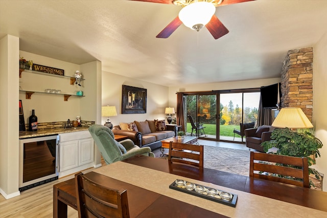 living room with light hardwood / wood-style flooring, ceiling fan, bar area, and beverage cooler