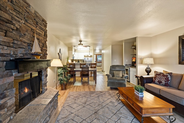 living room with hardwood / wood-style floors, a textured ceiling, a fireplace, and ceiling fan