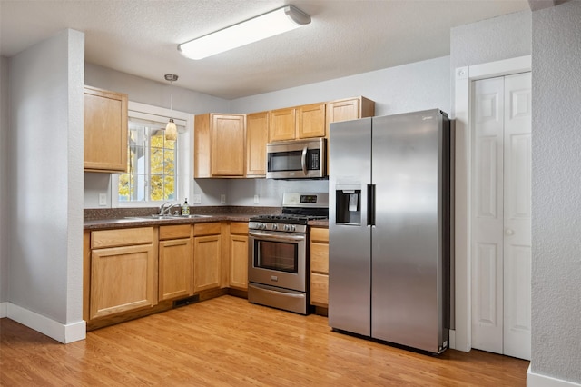 kitchen with a textured ceiling, stainless steel appliances, sink, pendant lighting, and light hardwood / wood-style floors