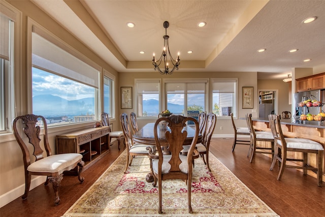 dining area with a chandelier, dark hardwood / wood-style flooring, a mountain view, and a tray ceiling