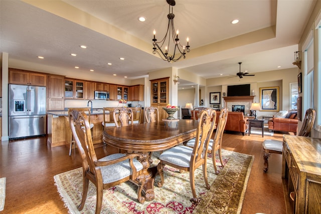 dining area with ceiling fan with notable chandelier, dark hardwood / wood-style floors, a raised ceiling, and sink