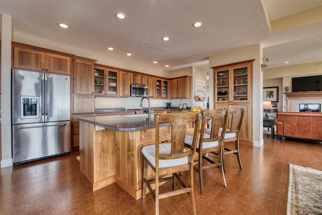 kitchen featuring appliances with stainless steel finishes, a textured ceiling, a kitchen island with sink, sink, and a breakfast bar area