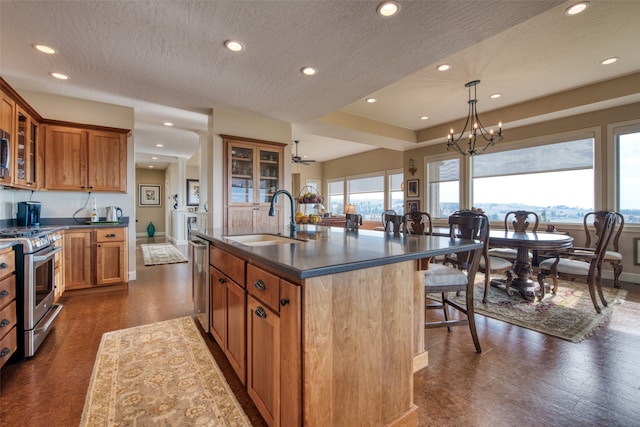 kitchen with a center island with sink, sink, hanging light fixtures, a textured ceiling, and stainless steel appliances