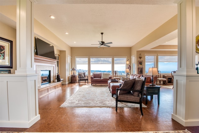 living room with a fireplace, a textured ceiling, ornate columns, and ceiling fan