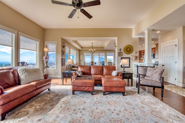 living room featuring ceiling fan with notable chandelier, decorative columns, and a raised ceiling