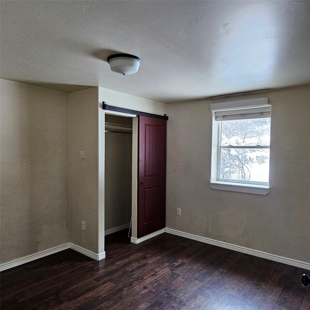 unfurnished bedroom with dark wood-type flooring, a barn door, and a closet